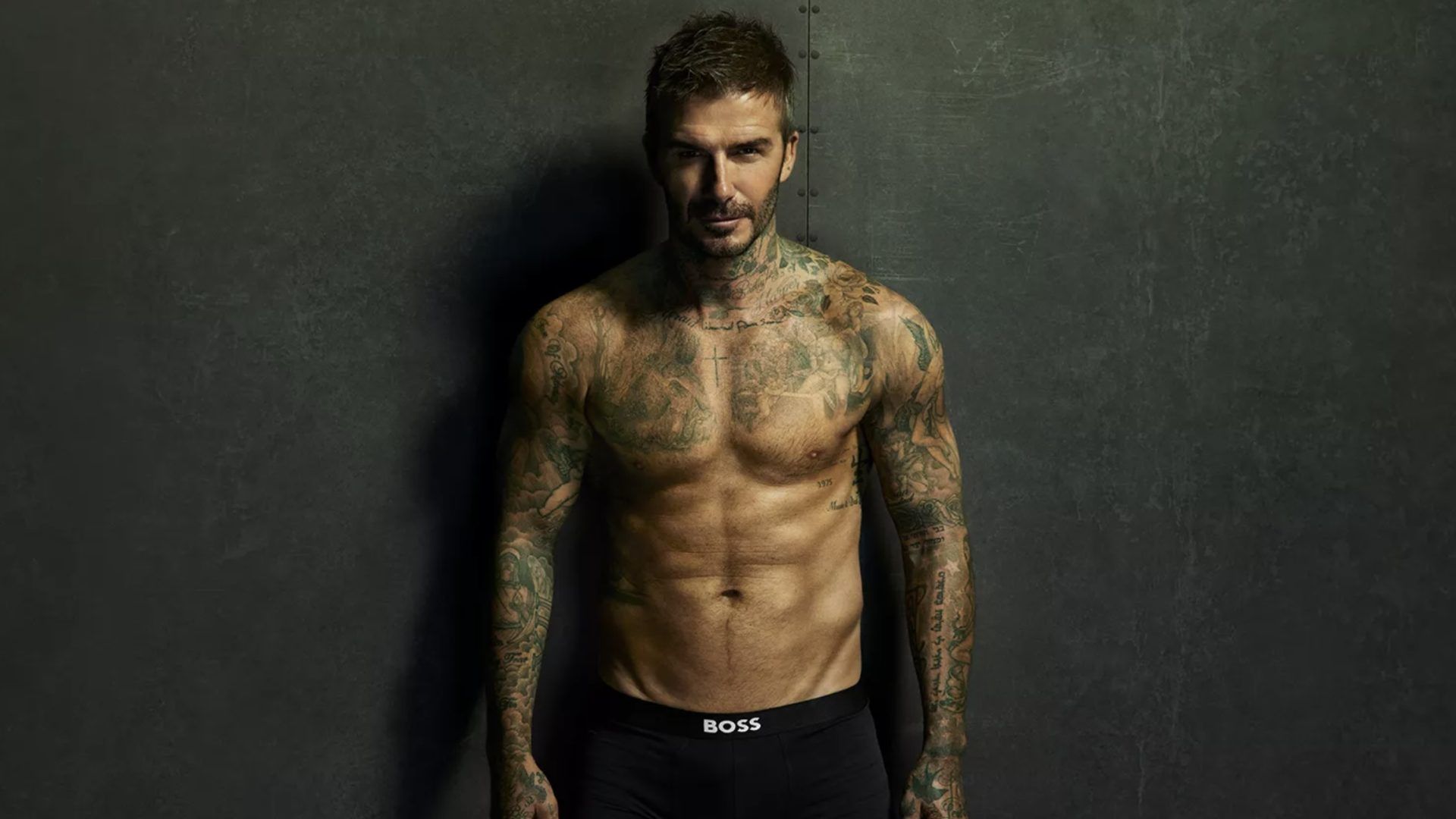 David Beckham în boxeri negri stă sprijinit de perete, abdomen sculptat