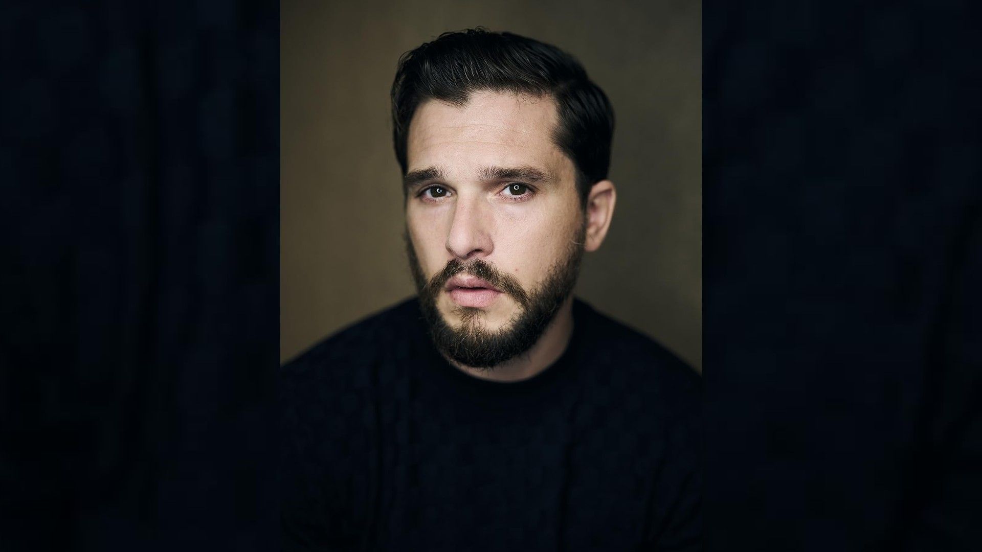 Portretul actorului Kit Harington: poartă un tricou negru, tunsoare stilată, barbă îngrijită