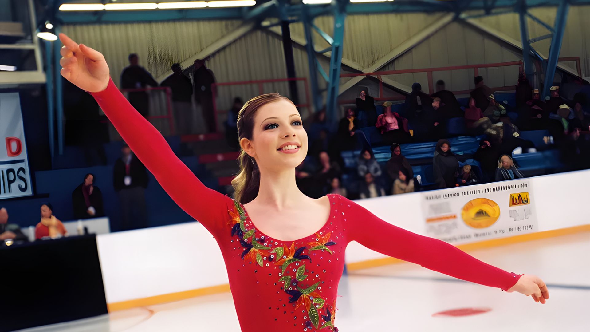 Michelle Trachtenberg într-un costum roșu de patinaj dansează pe gheață, cu brațele ridicate