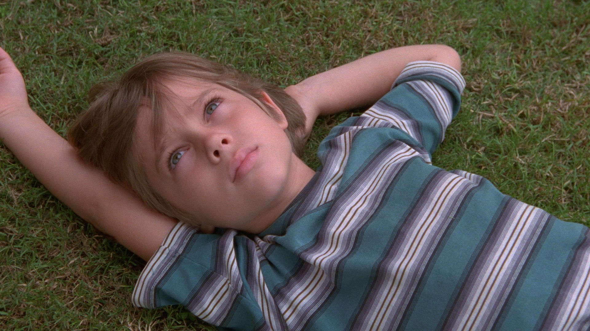 O imagine din filmul "Boyhood": tânărul Ellar Coltrane într-un tricou în dungi stând întins pe iarbă