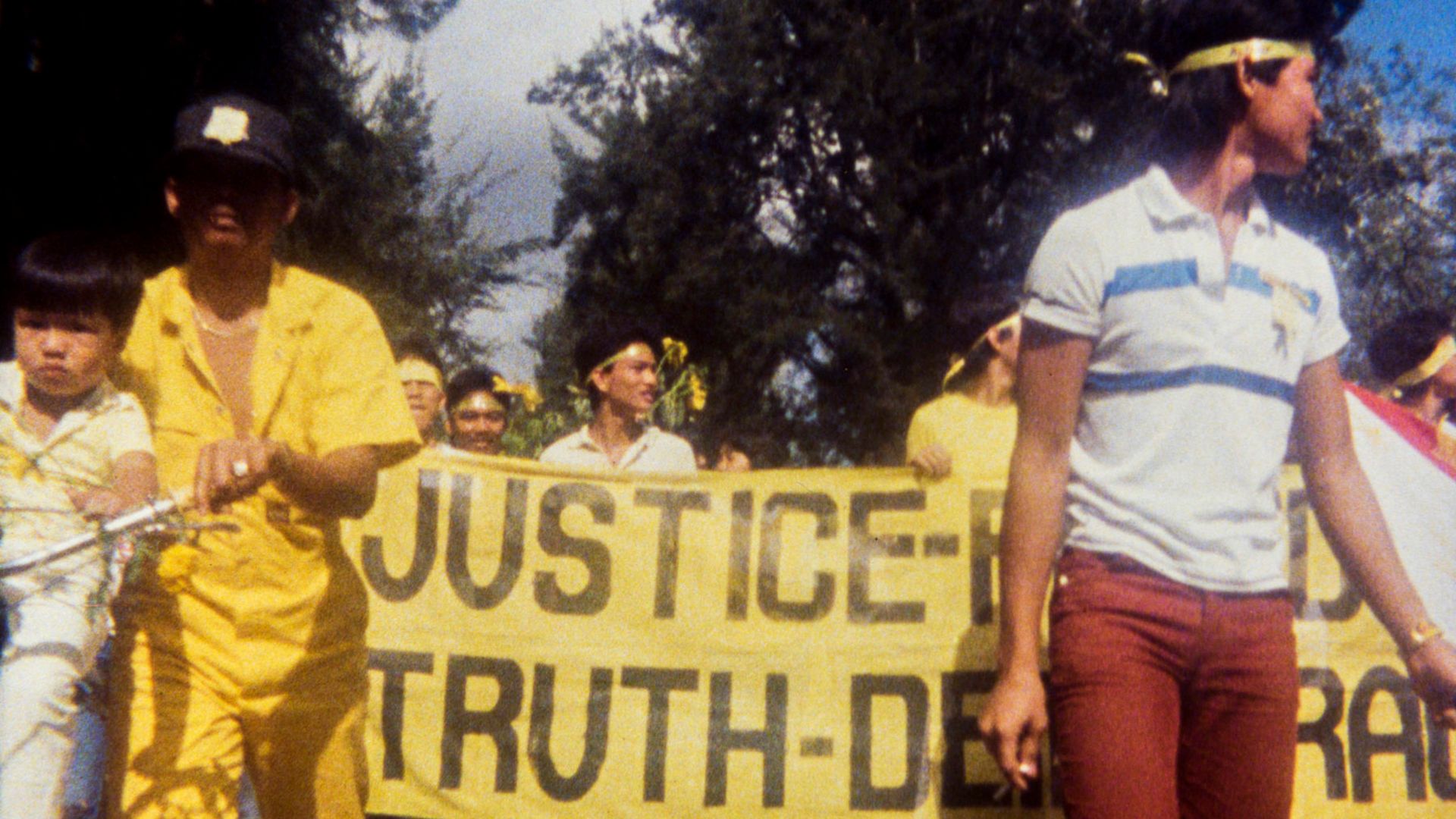 Cadru din filmul „Why is Yellow the Middle of the Rainbow?”: un grup de oameni cu un poster galben la o demonstrație