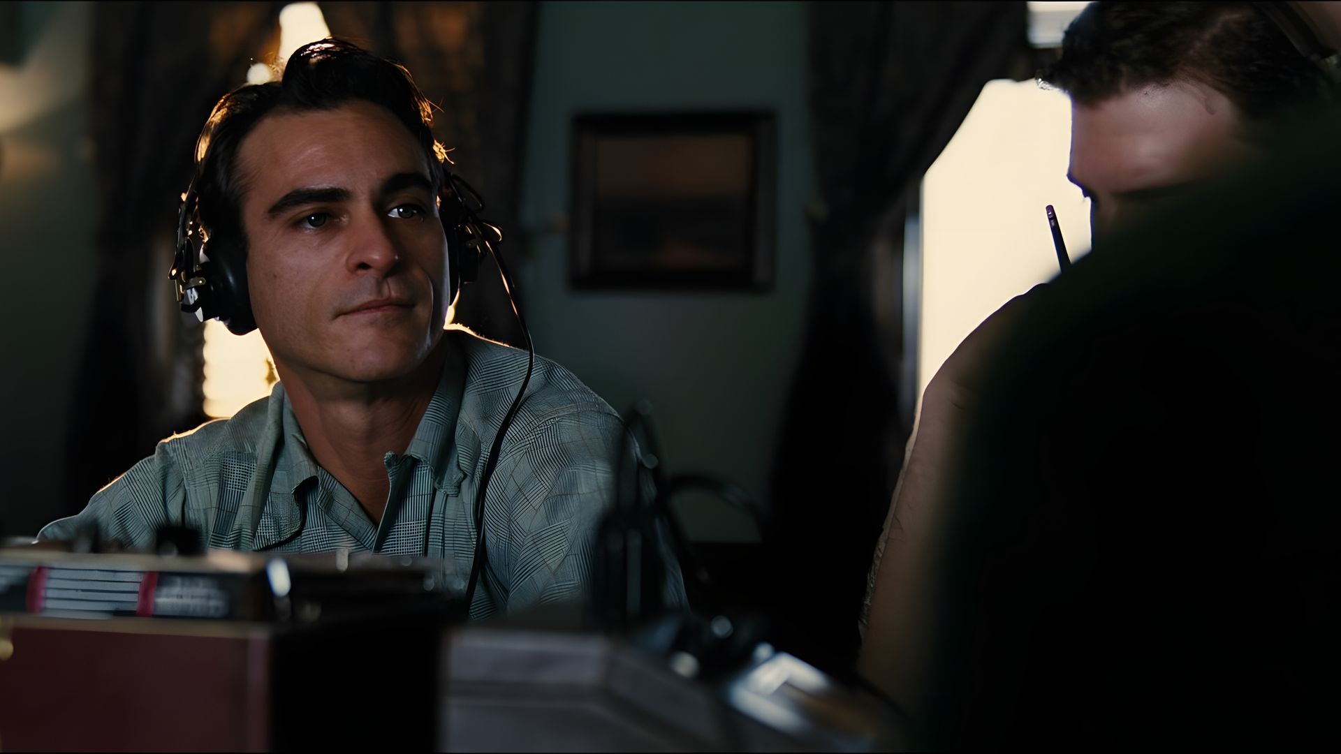 Joaquin Phoenix într-o cămașă albastră și căști mari, privind în depărtare