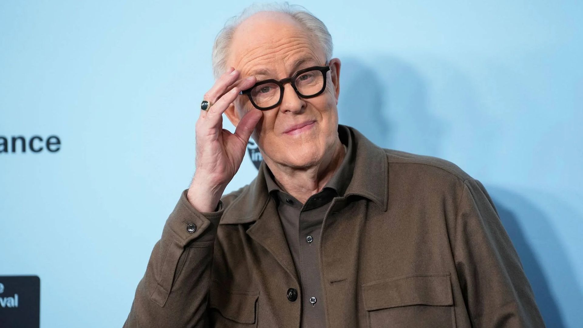 Actorul John Lithgow își ajustează ochelarii într-o ramă neagră