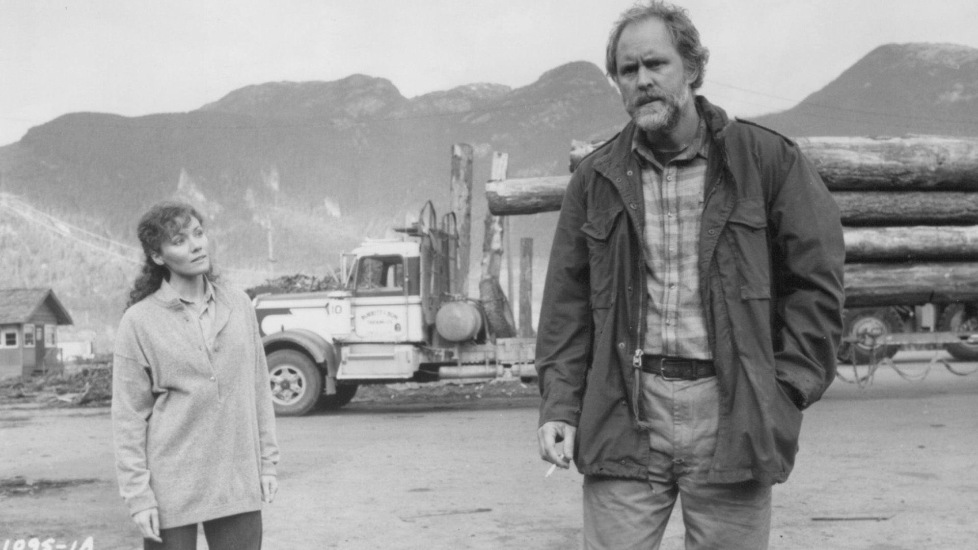 John Lithgow în haine rupte stă pe fundalul unui camion forestier într-o scenă din filmul "Distant Thunder"