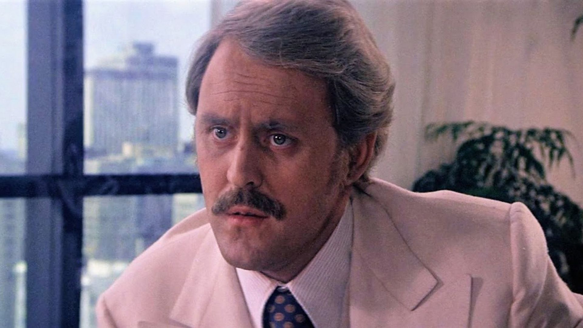 John Lithgow cu mustață și într-o jachetă crem într-o scenă din filmul "Obsession"