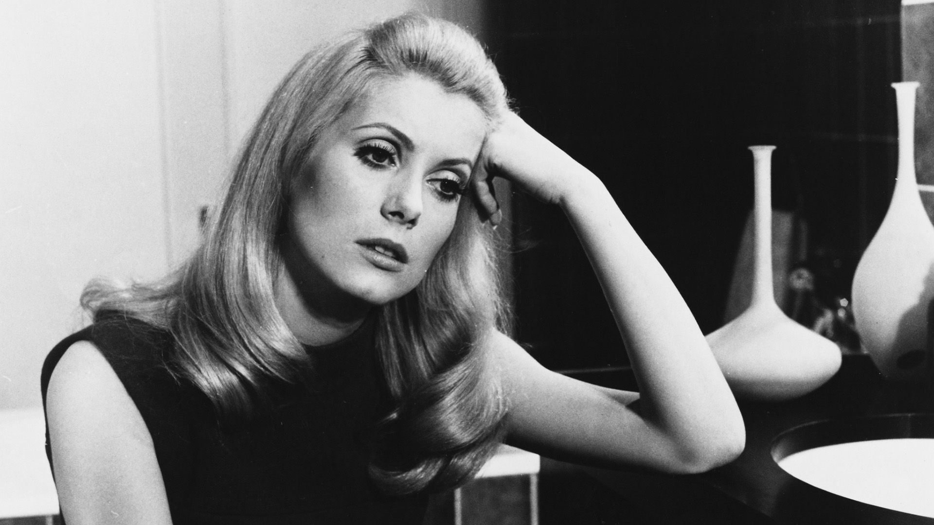 Catherine Deneuve se sprijină gânditoare de masă într-o scenă din filmul 'Belle de Jour'