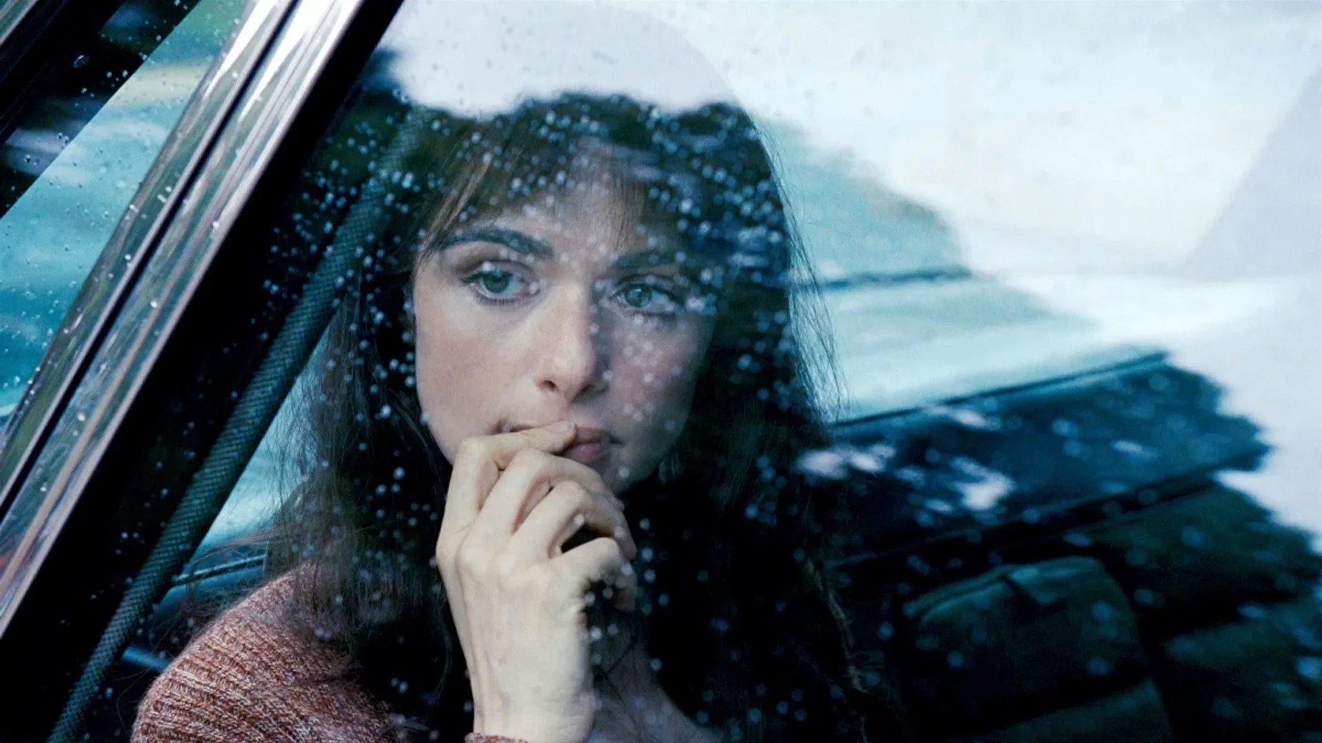 Prim-plan cu fața actriței Rachel Weisz filmată prin geamul unei mașini în timp ce plouă