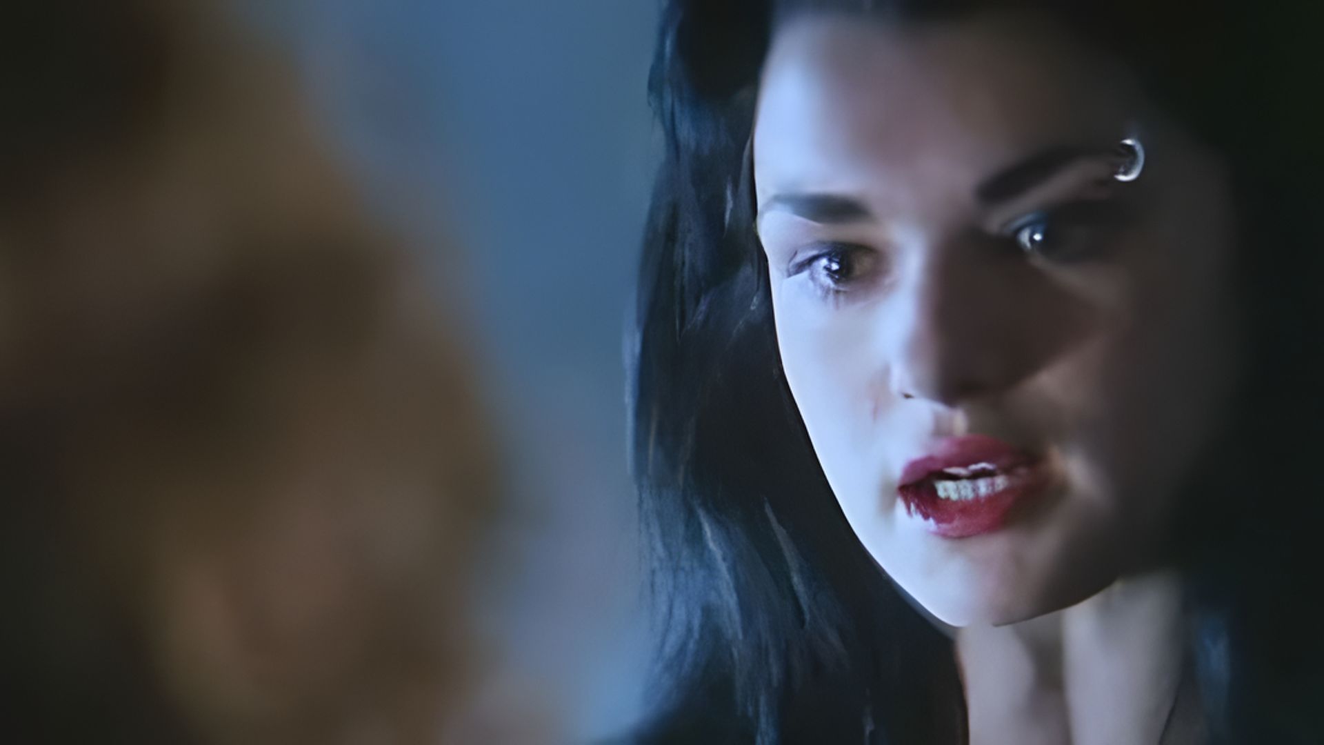 Un prim-plan al feței lui Rachel Weisz, are rujul roșu aprins și un inel în sprânceană