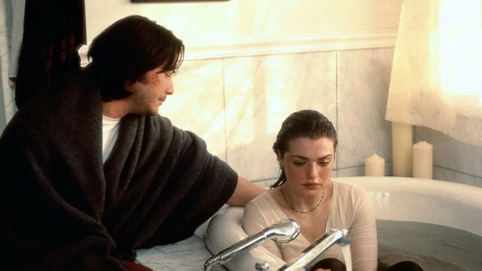 Tânăra Rachel Weisz stă în cadă îmbrăcată, lângă ea stă tânărul Keanu Reeves