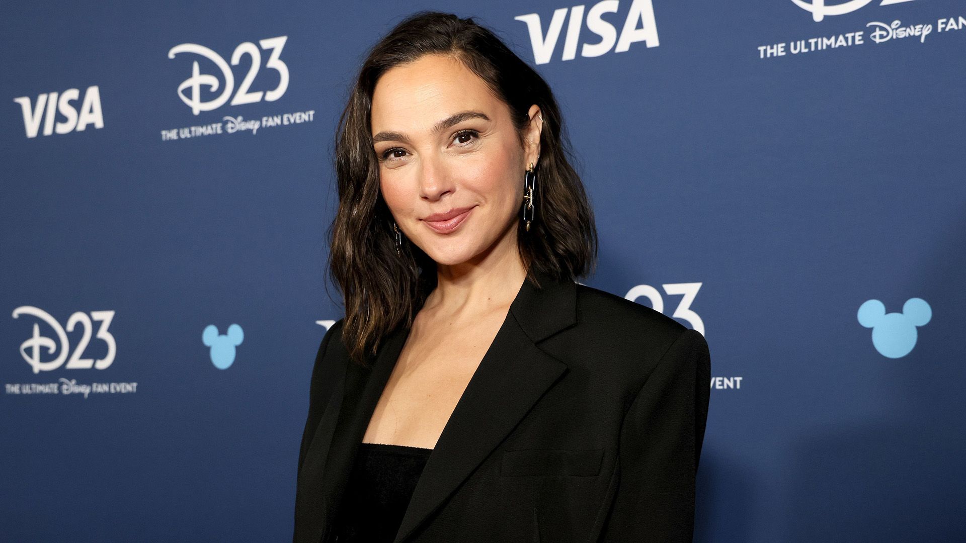 Actrița Gal Gadot într-o jachetă neagră pe un fundal albastru