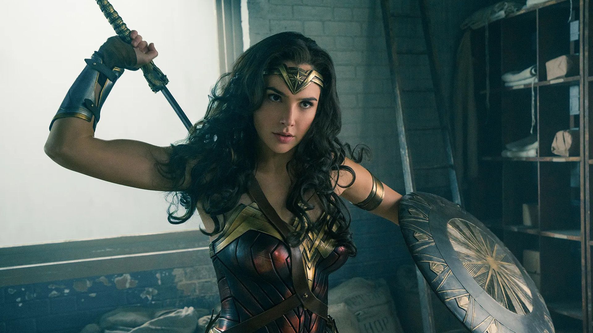 Gal Gadot ca Wonder Woman: în armură, ținând un scut cu mâna stângă, scoțând o sabie din spatele ei cu mâna dreaptă