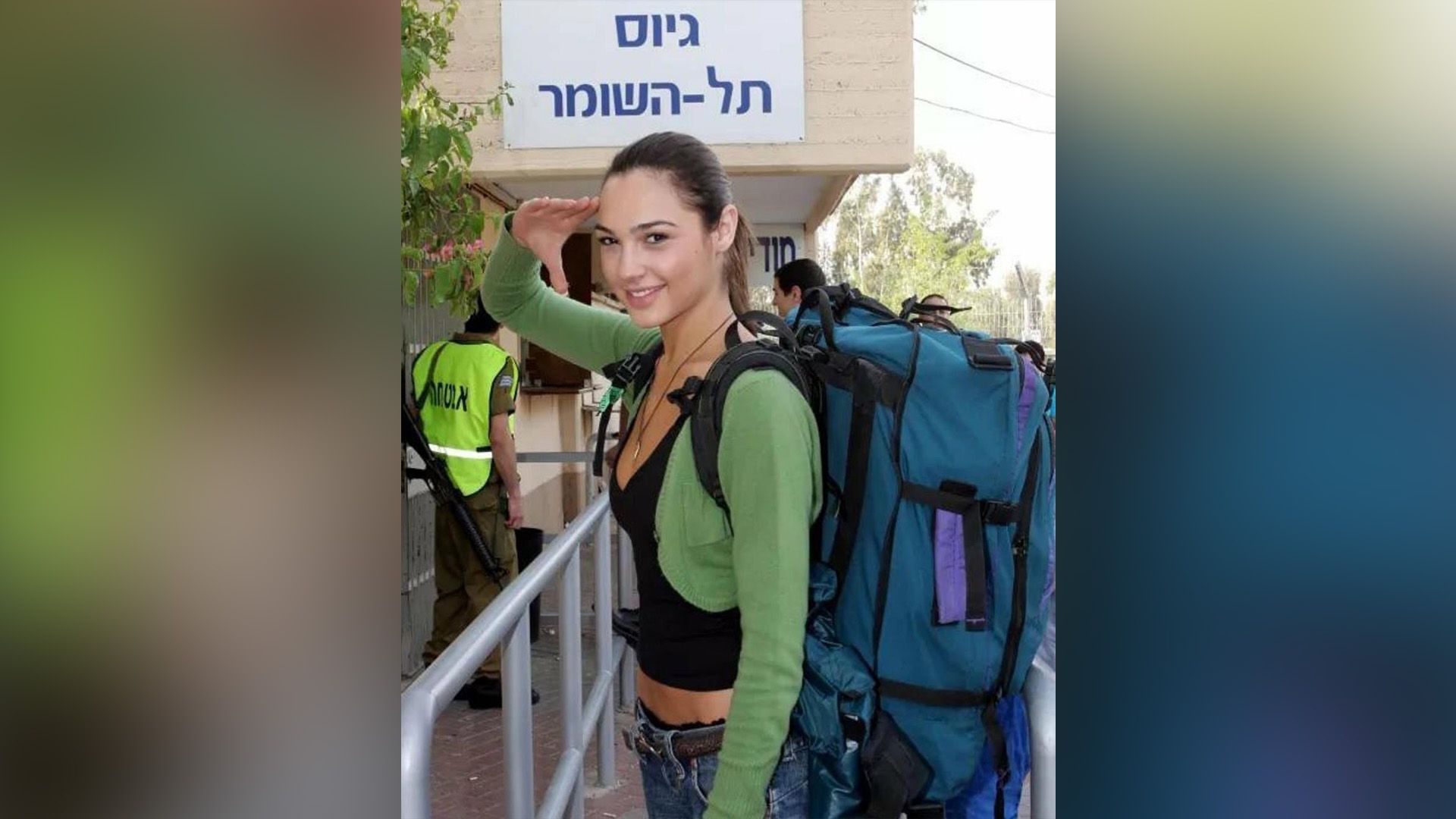 Young Gal Gadot in a green sweater and with a large blue backpack on her back is saluting with her right hand