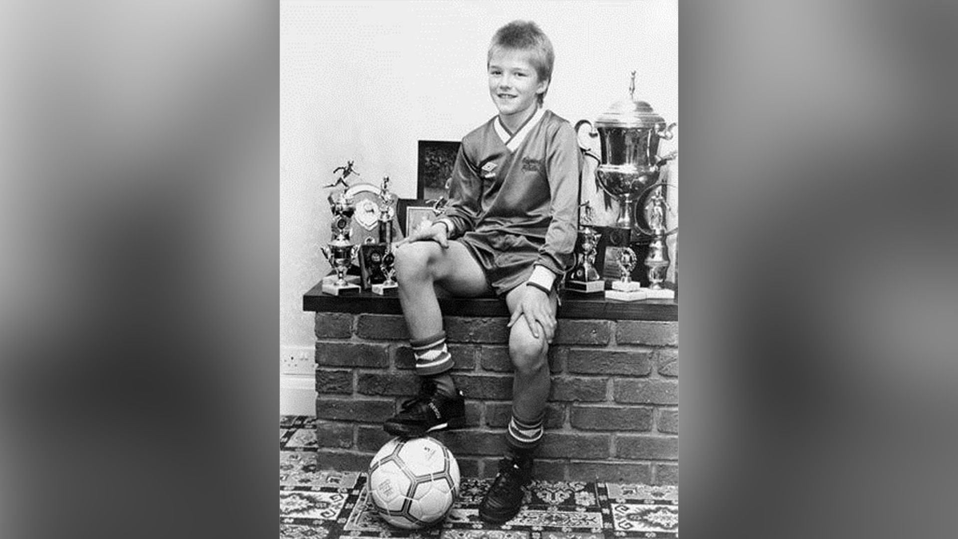 David Beckham copil îmbrăcat în echipament de fotbal și cu o minge de fotbal