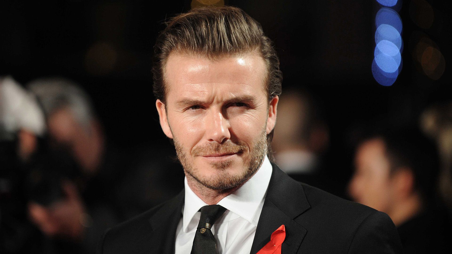 Fotbalistul David Beckham într-o jachetă neagră cu o panglică roșie prinsă de ea