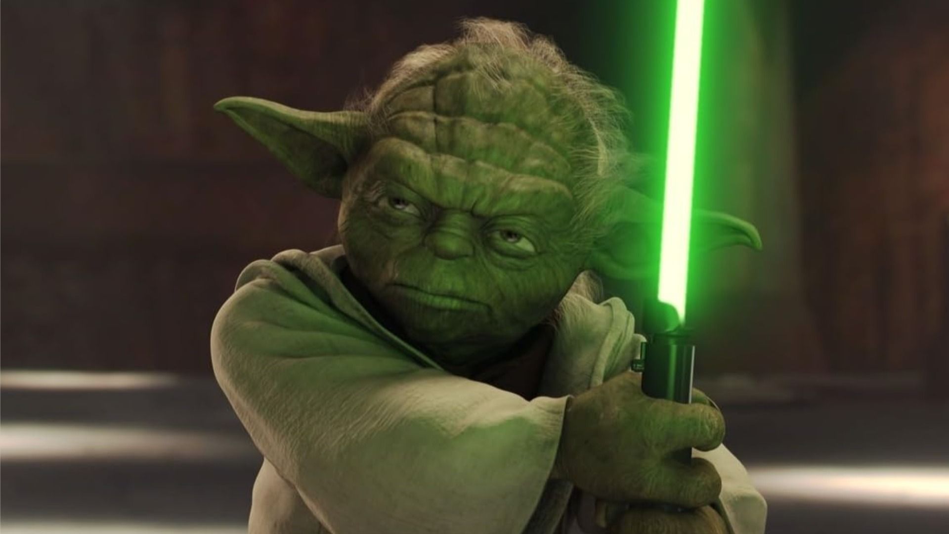 Maestrul Yoda ține un lightsaber și privește sever într-o parte pe un fundal maro
