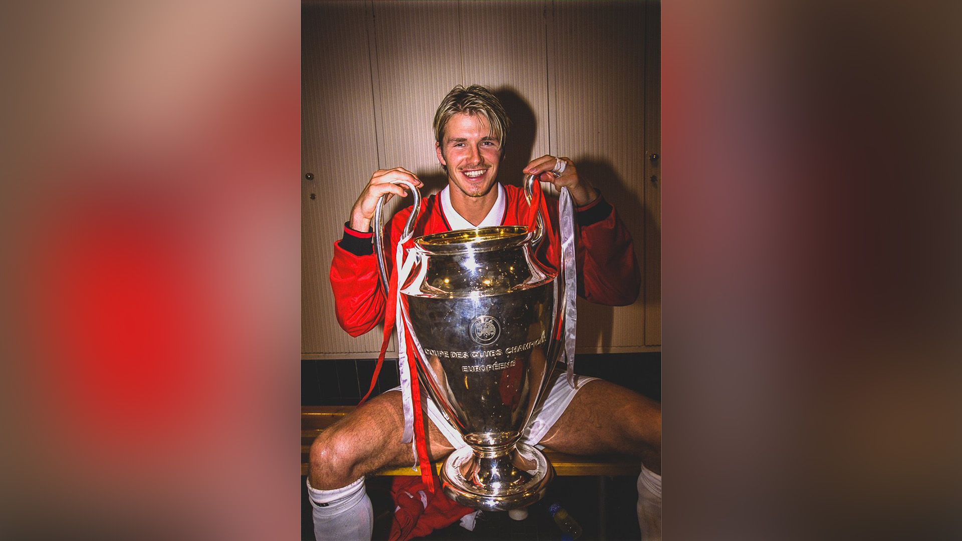 Tânărul David Beckham așezat pe banca vestiarului sportiv cu Cupa UEFA