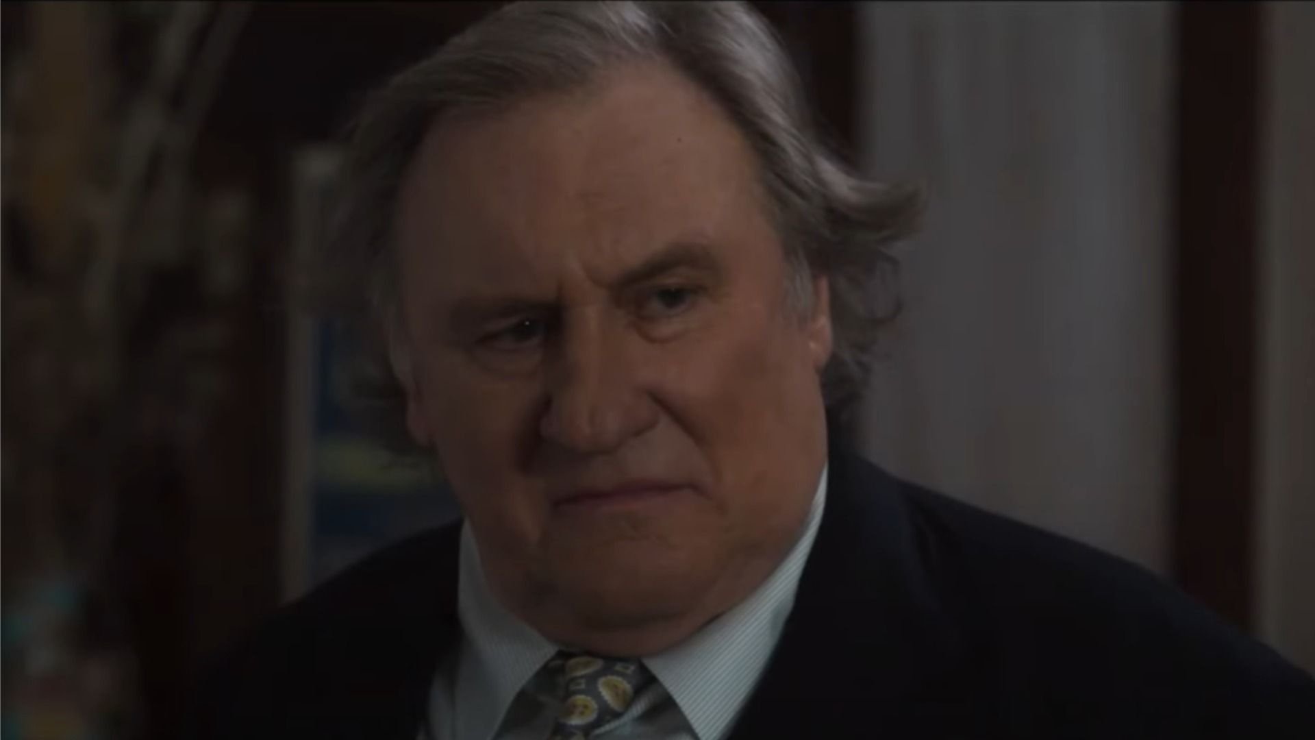 Actorul Gérard Depardieu într-un costum clasic privește lateral pe un fundal blurat