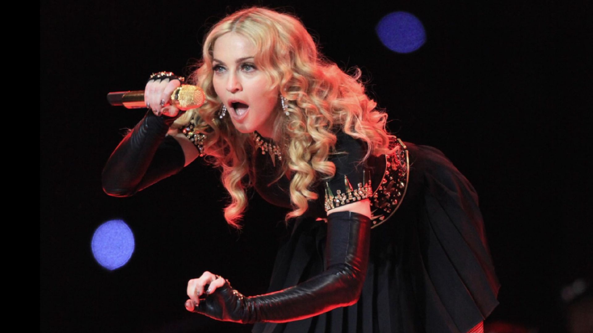 Madonna cântă la microfon, aplecându-se înainte