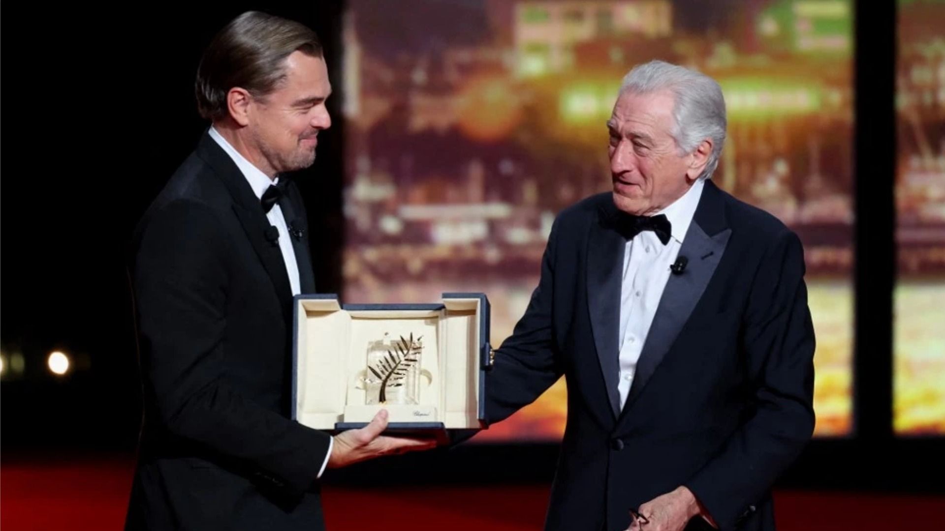 Actorul Leonardo DiCaprio zâmbește în timp ce îi înmânează lui Robert De Niro 'Palme d'Or' pe scenă