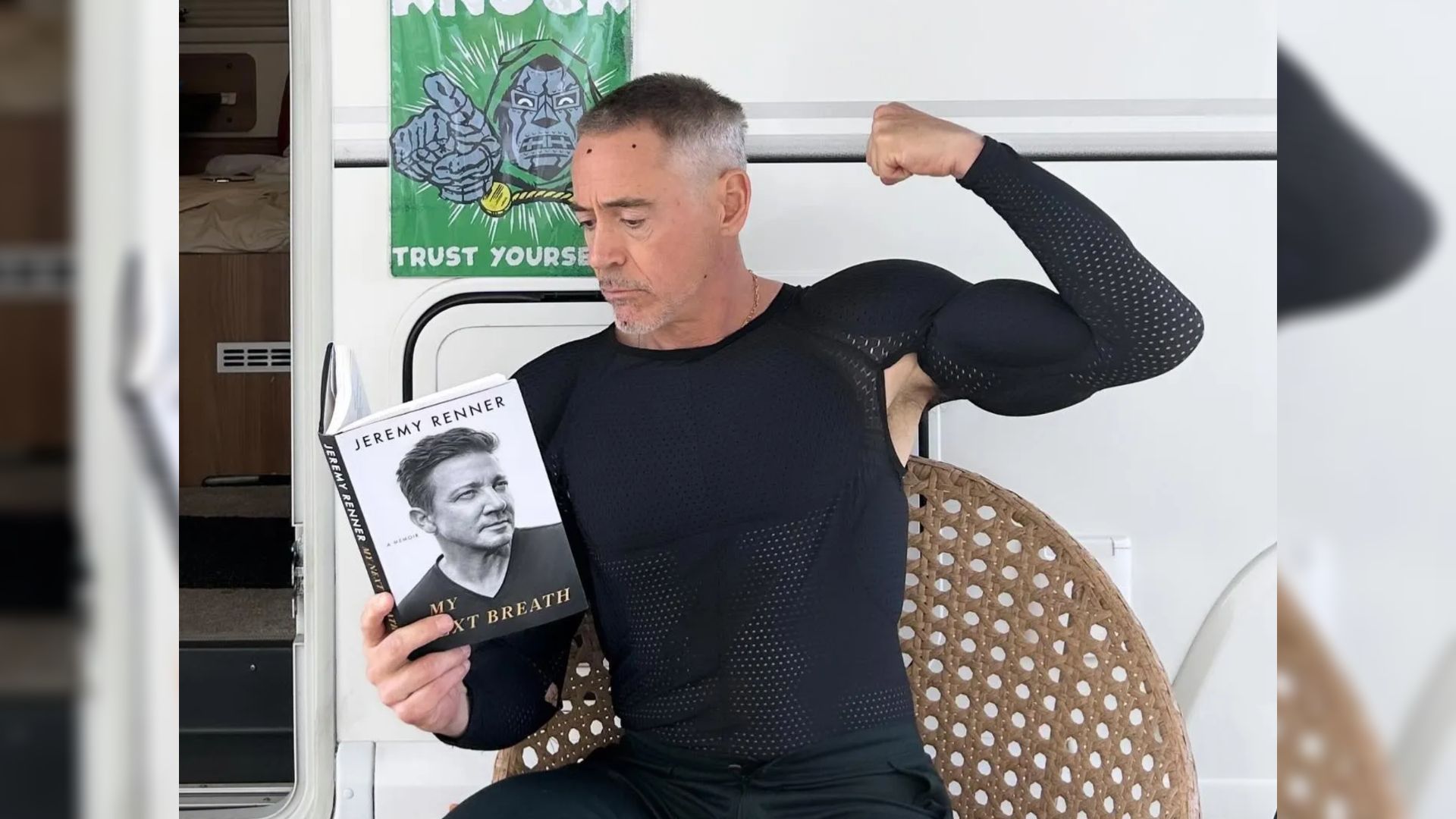 Actorul Robert Downey Jr. în haine strâmte stă lângă o rulotă și ține o carte în mâini