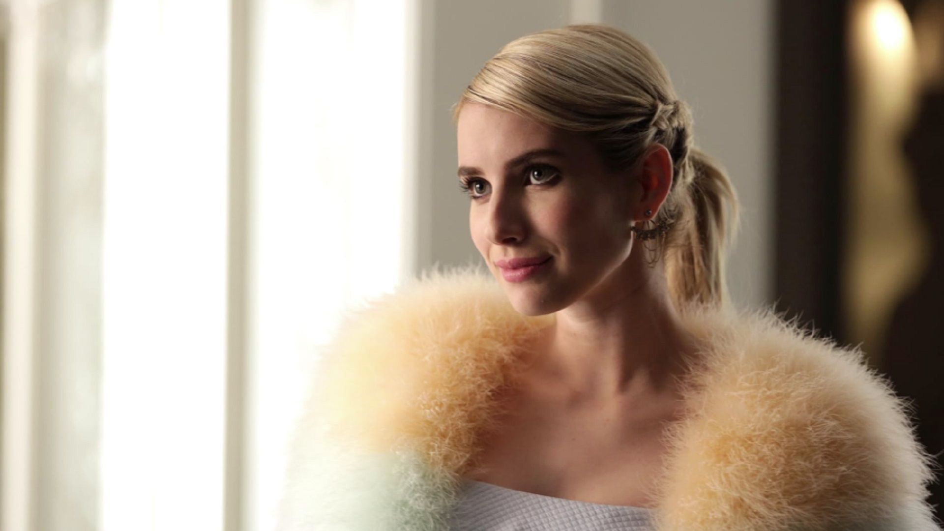 Emma Roberts în pelerină de blană privește dulce spre stânga