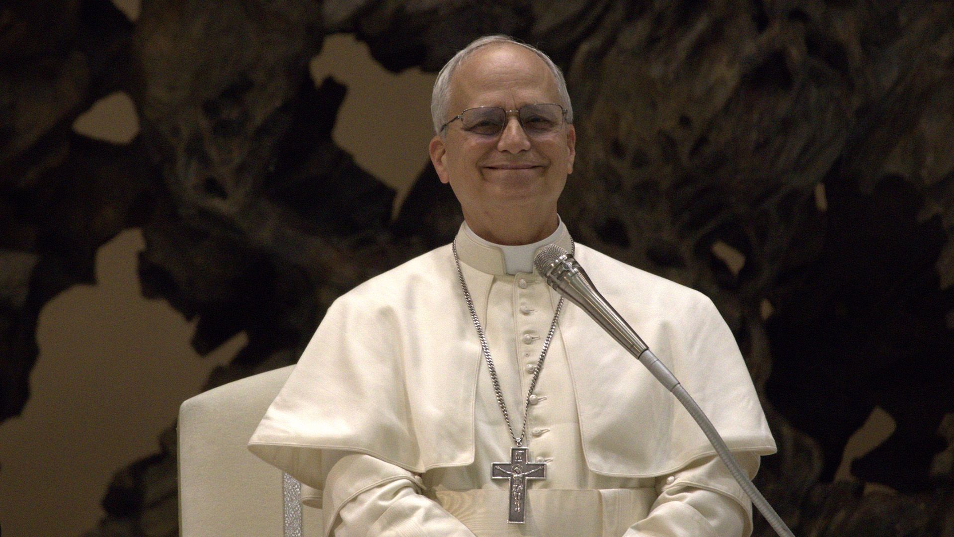 Papa Leon al XIV-lea zâmbitor în haine albe pe un fundal întunecat