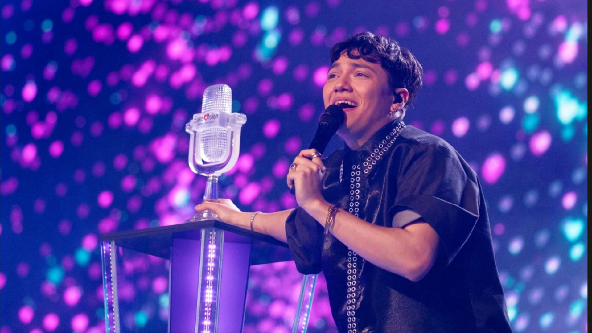 Cântărețul JJ stă pe scenă lângă piedestal cu statueta concursului Eurovision 2025 și zâmbește