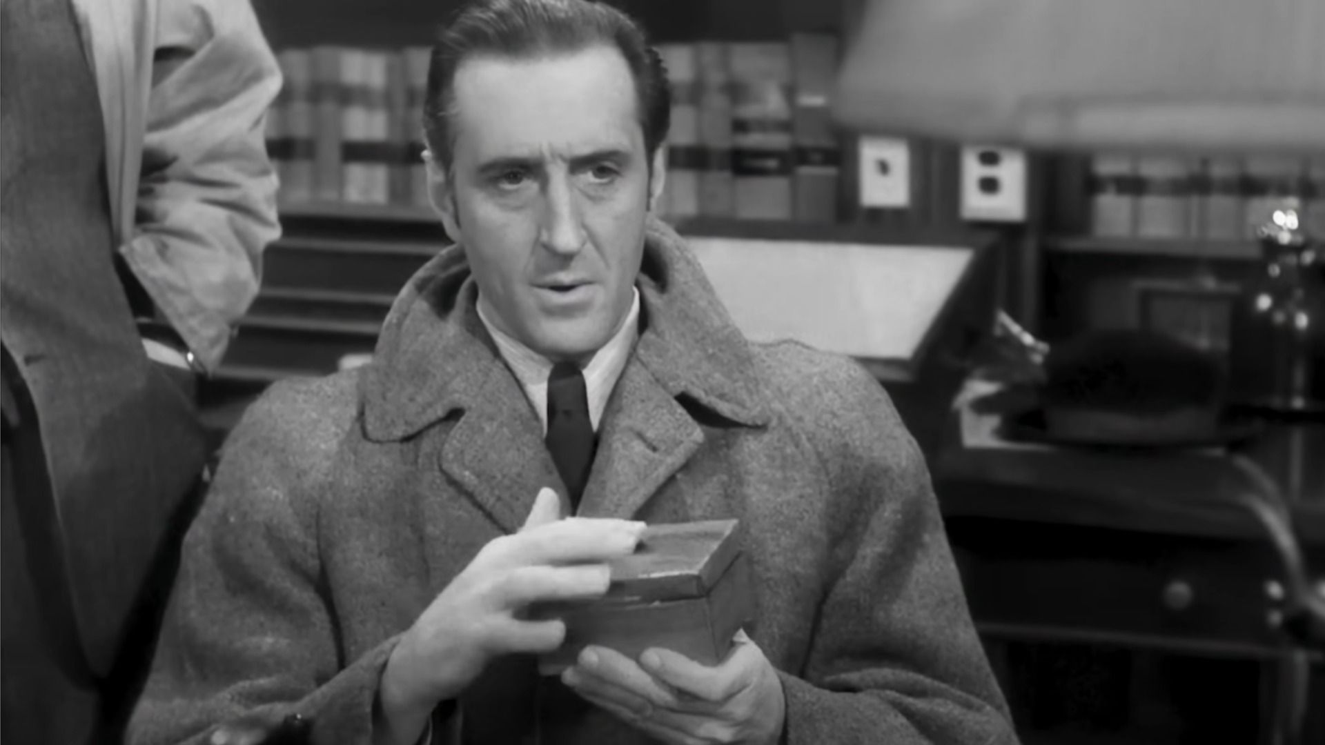 Actorul Basil Rathbone în rolul Sherlock Holmes ține o cutie în mâini și privește în jos