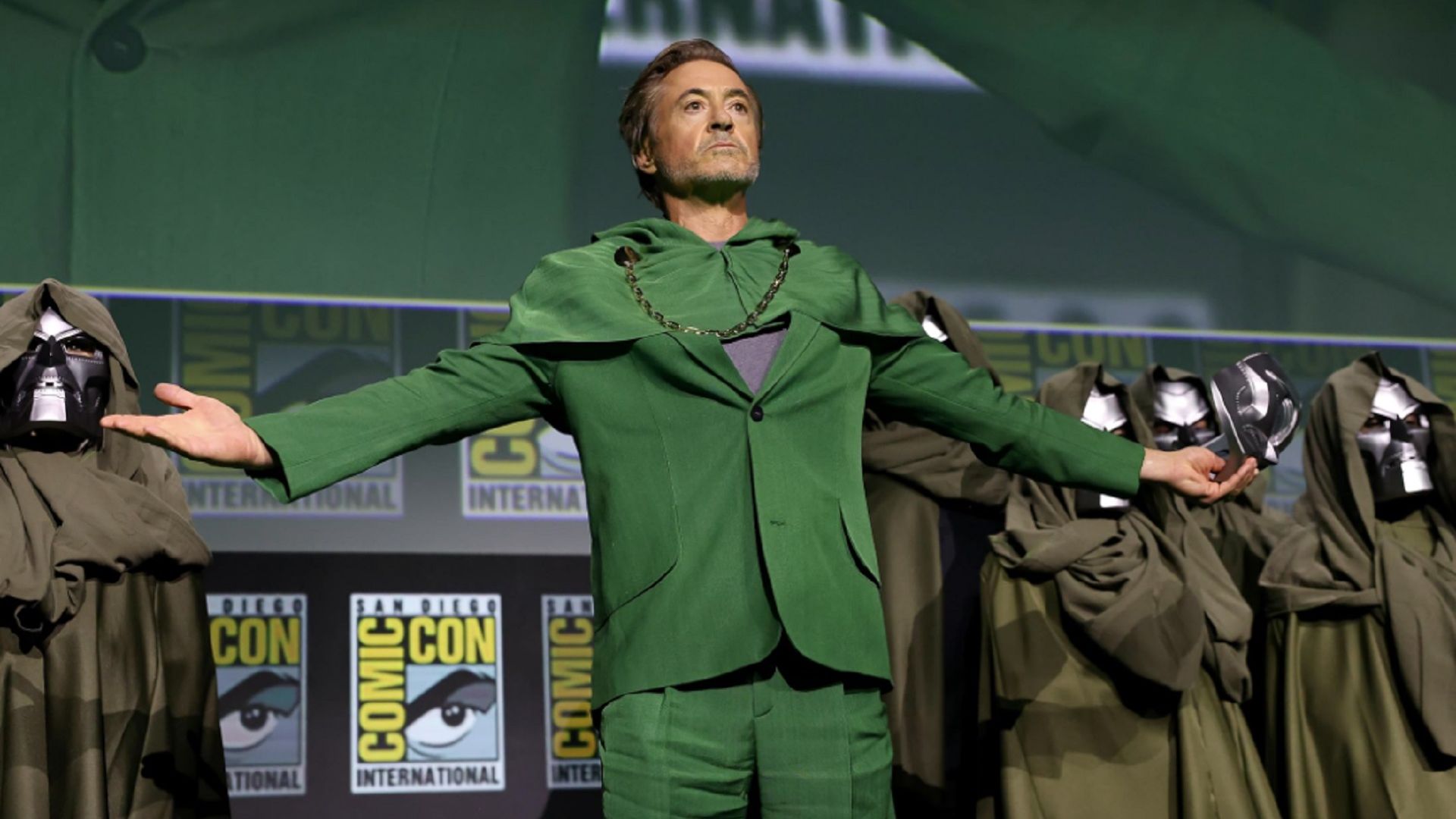 Robert Downey Jr. într-un costum verde stă pe scenă, cu brațele întinse