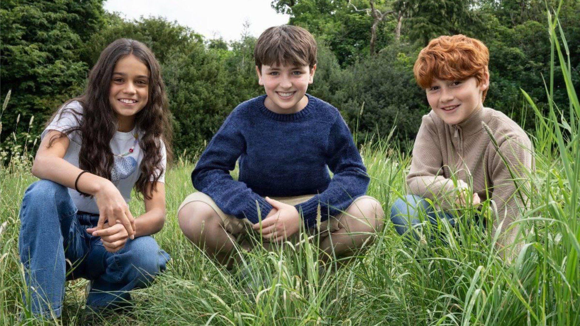 Actorii Dominic McLaughlin, Alastair Stout și Arabella Stanton stând pe iarbă și zâmbind