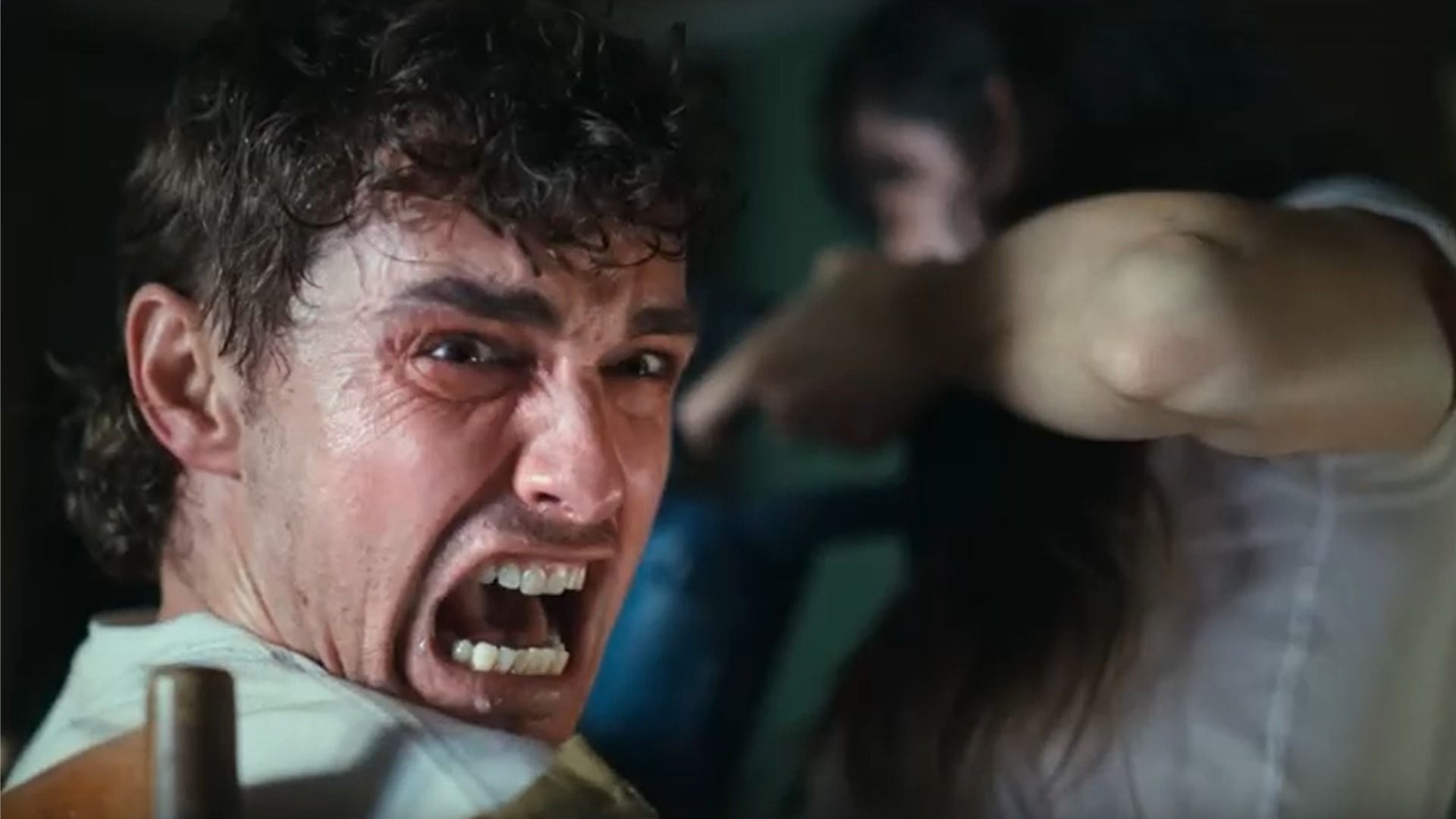 Actorul Dave Franco se uită în lateral și strigă în timp ce stă pe un scaun lângă actrița Alison Brie