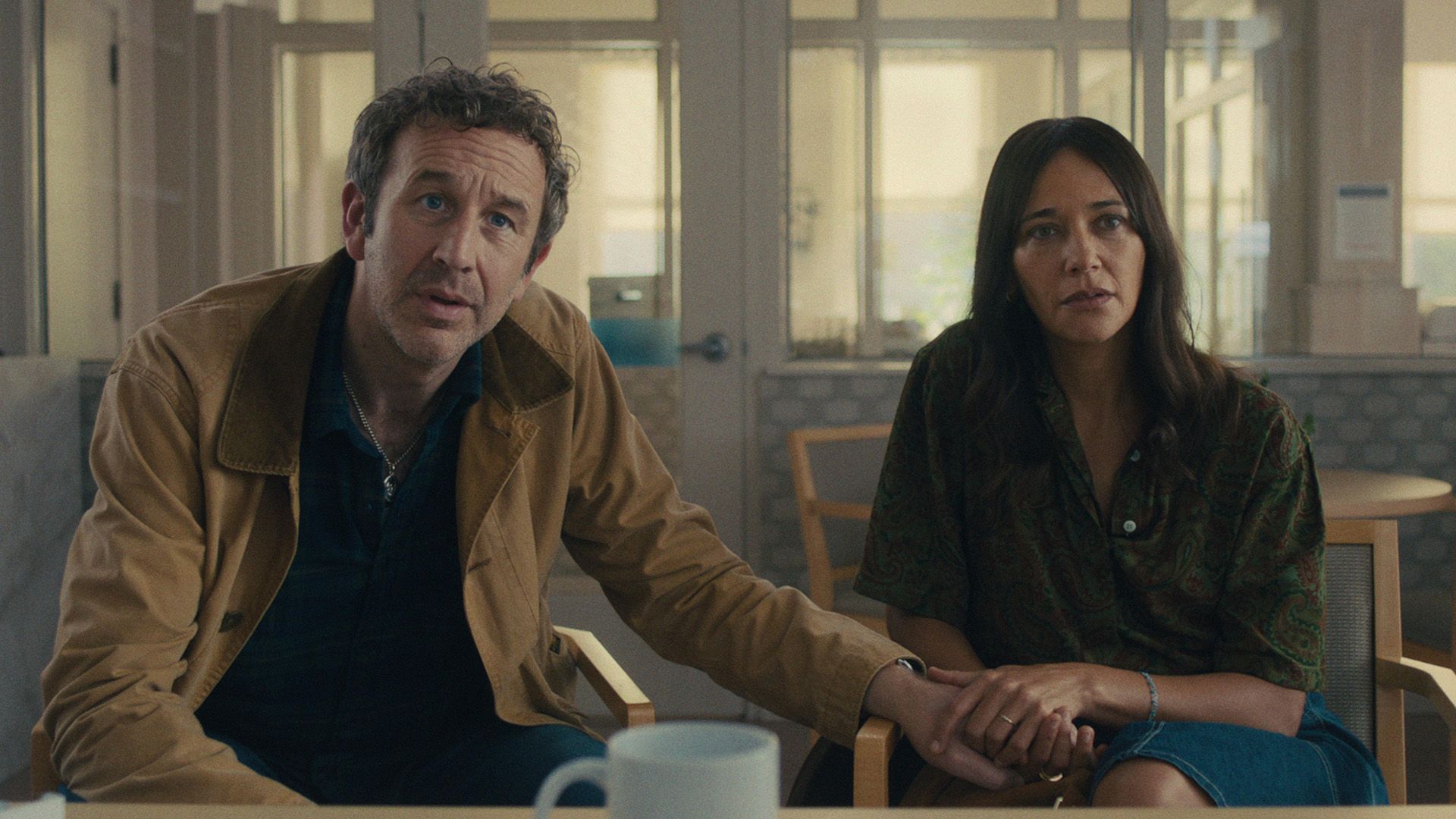Chris O'Dowd și Rashida Jones stând pe scaune cu expresii îngrijorate, ținându-se de mâini