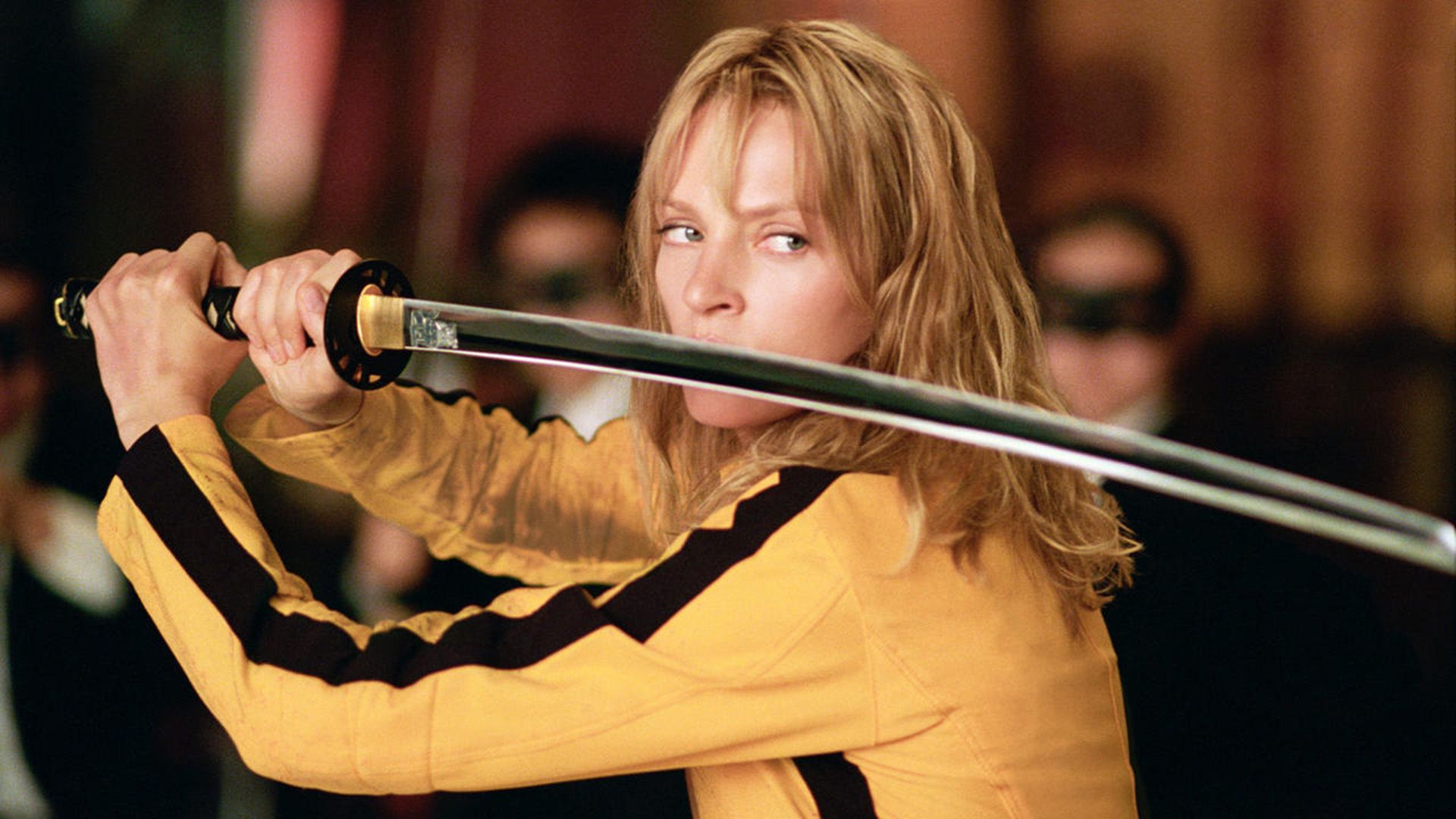 Uma Thurman într-un pulover galben cu dungi negre ține o katana în fața feței în 'Kill Bill'