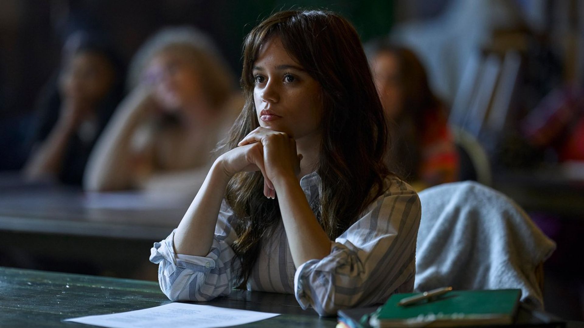Jenna Ortega într-un pulover alb stă la bancă în timpul orei cu o expresie concentrată