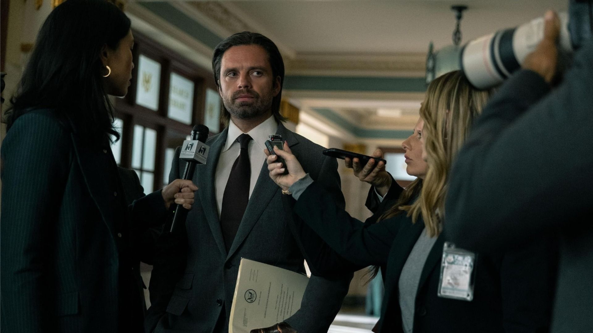 Actorul Sebastian Stan într-un costum negru cu părul lung înconjurat de jurnaliști