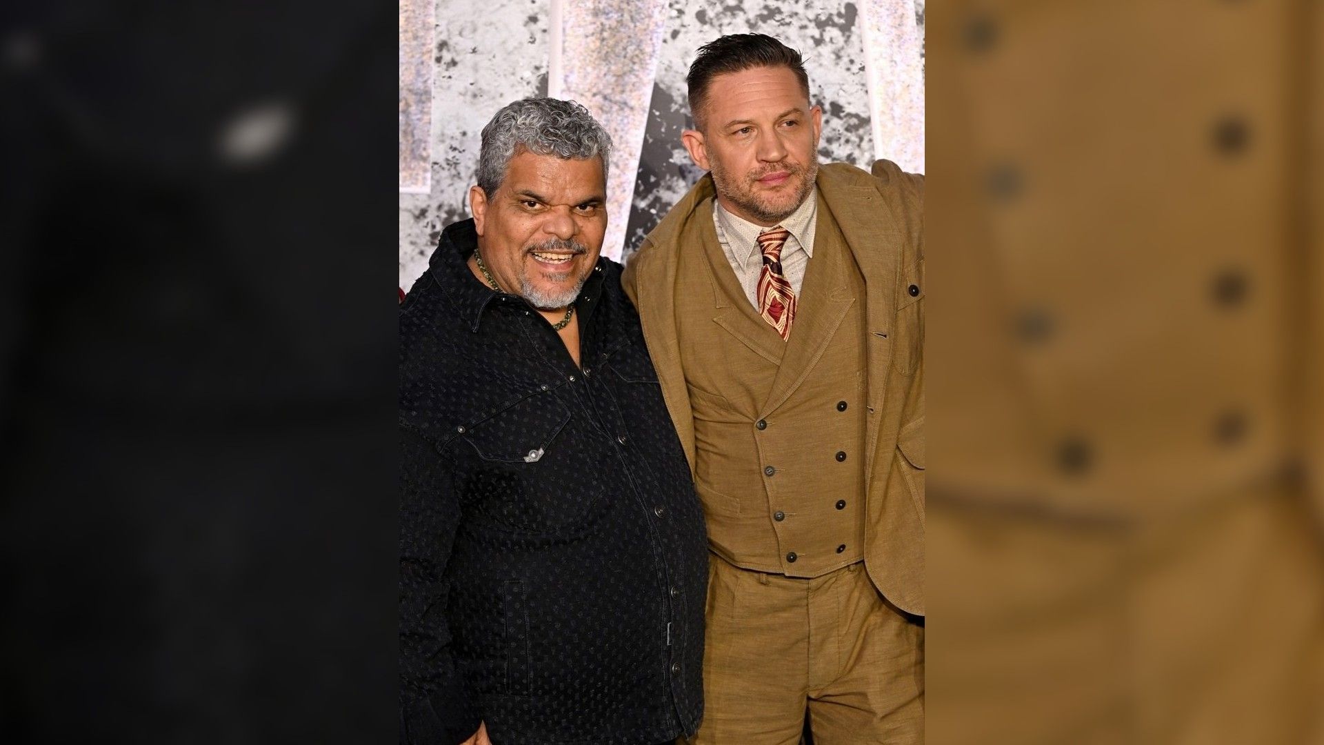Luis Guzmán și Tom Hardy pozează pe covorul roșu: unul în cămașă închisă, celălalt în costum maro cu cravată
