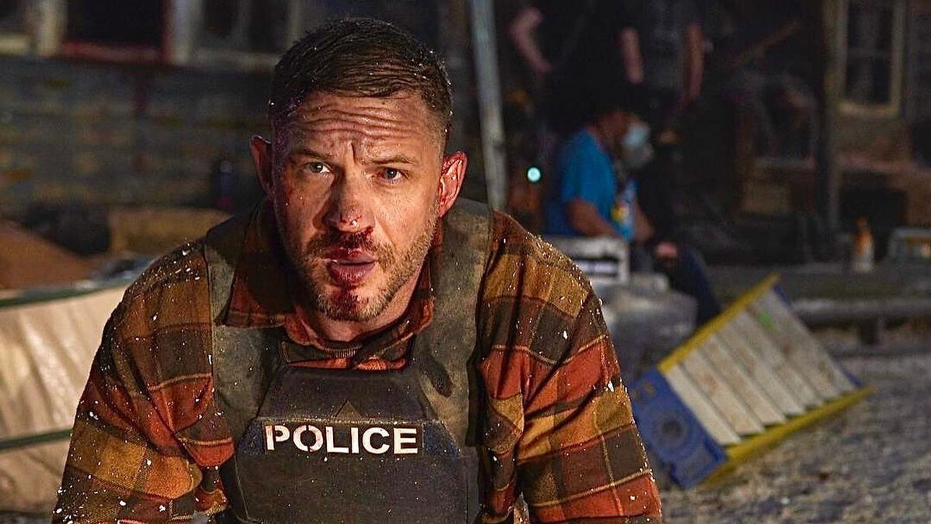 Tom Hardy într-o vestă antiglonț cu fața vânătă stă în genunchi la locul incidentului