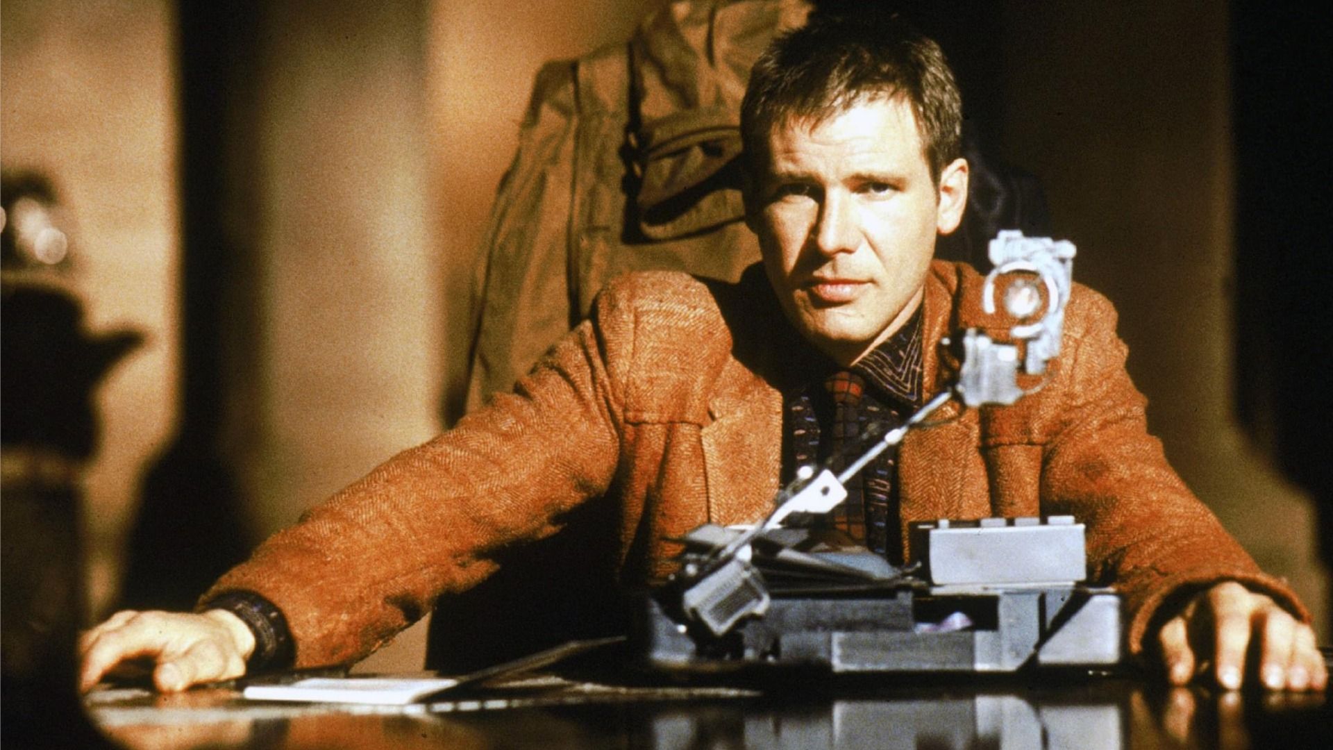 Actorul Harrison Ford în rolul lui Rick Deckard stă la masă într-o jachetă maro