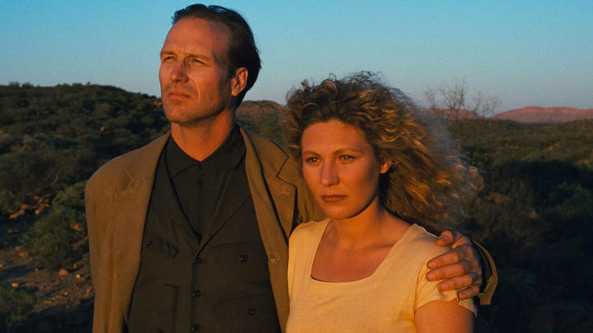 Actorul William Hurt într-o jachetă maro o îmbrățișează pe actrița Solveig Dommartin într-un tricou alb