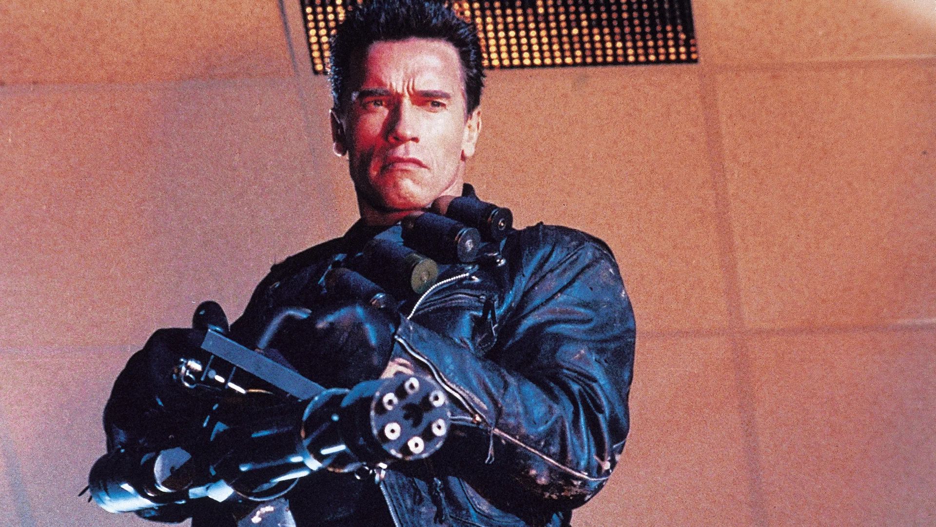 Arnold Schwarzenegger într-o jachetă de piele neagră ținând o mitralieră
