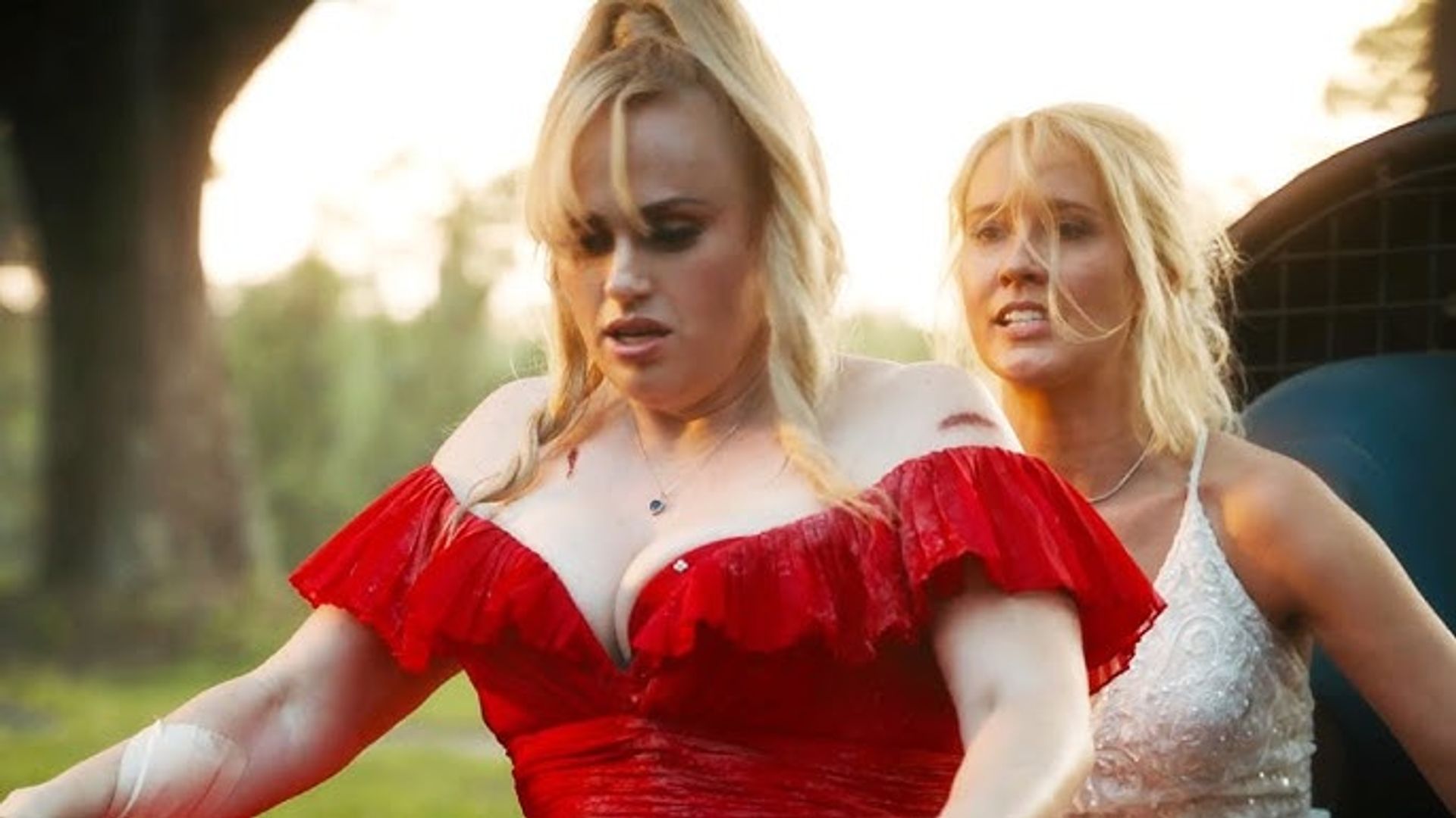 Rebel Wilson într-o rochie roșie și Anna Camp în alb mergând pe biciclete