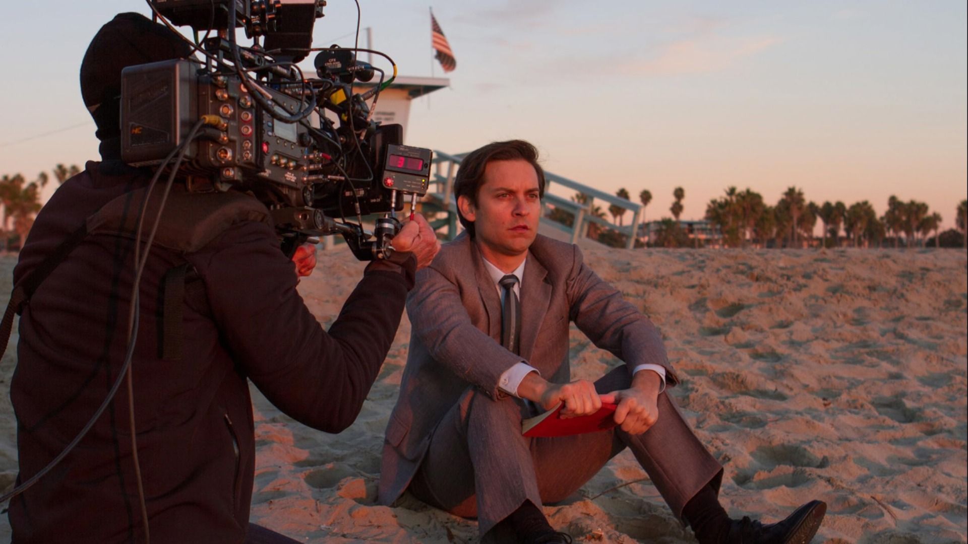 Actorul Tobey Maguire în costum gri stând pe nisip