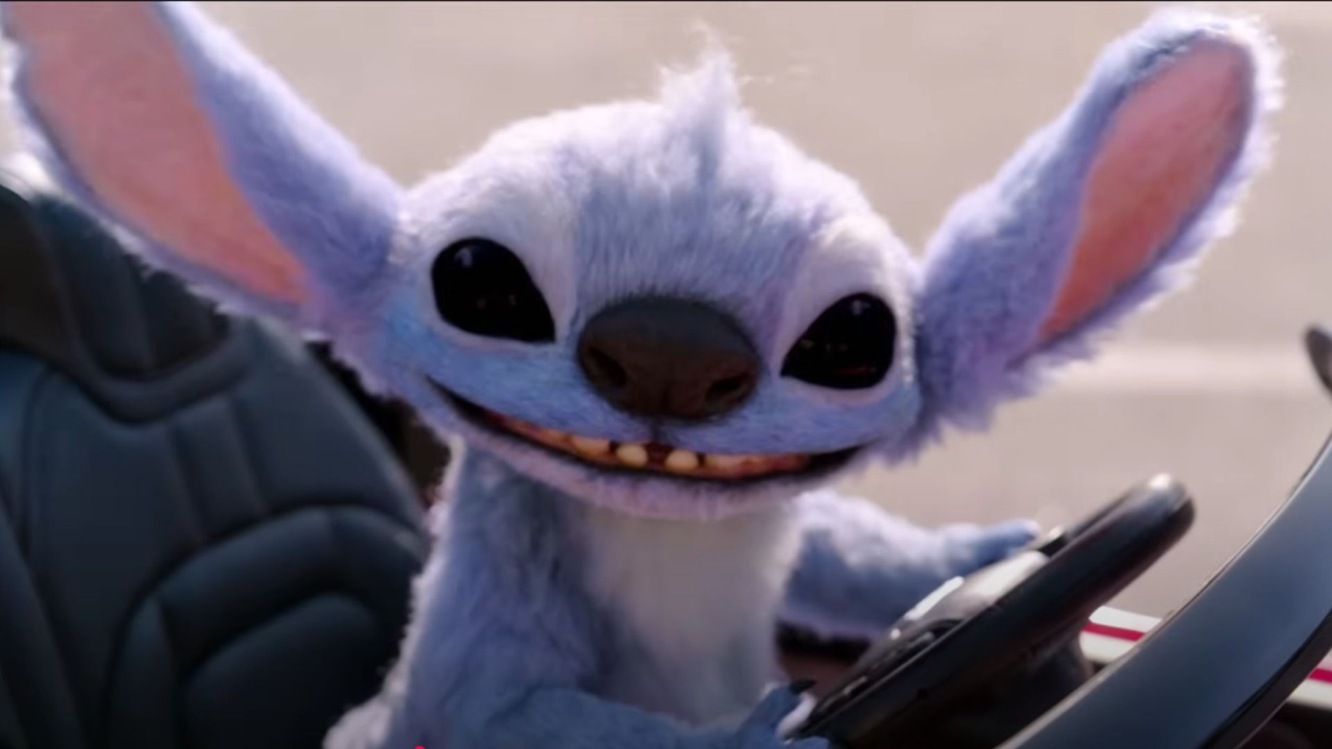 Alienul albastru Stitch stă la volanul unei mașini mici și zâmbește