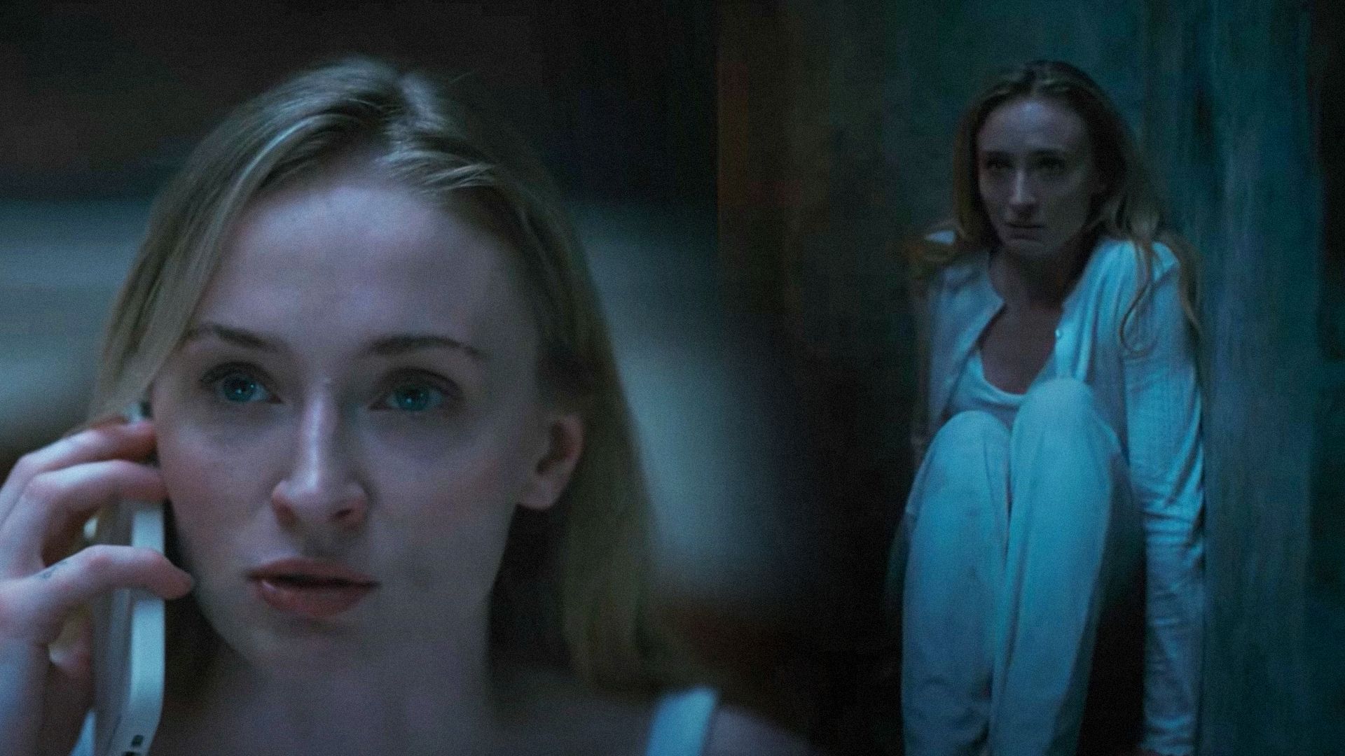 Actrița Sophie Turner cu un telefon în mână stând lângă perete într-o cămașă de noapte