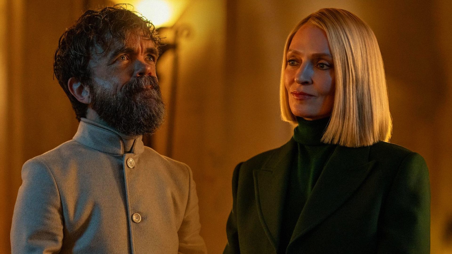 Actorul Peter Dinklage cu părul scurt și în haine albe, actrița Uma Thurman într-un blazer verde