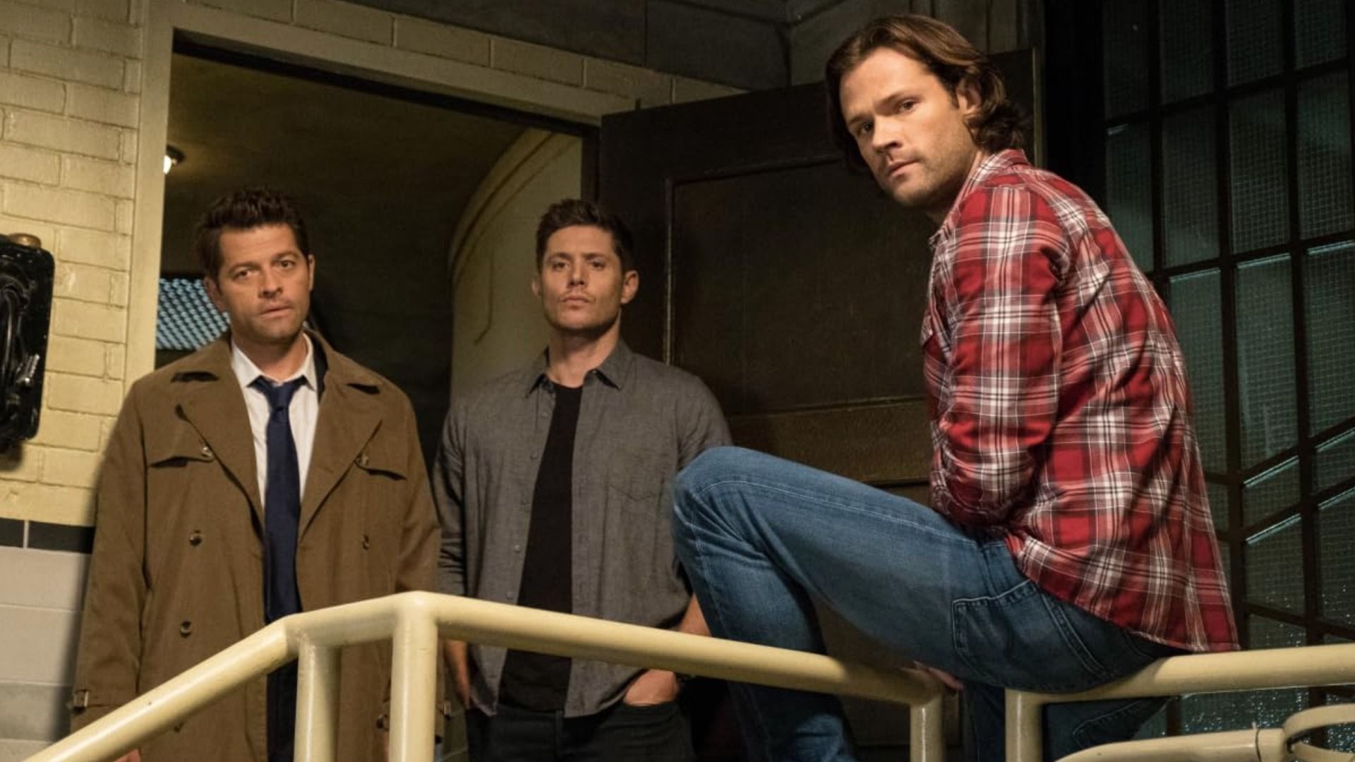 Actorii Misha Collins, Jensen Ackles și Jared Padalecki stau lângă ușă privind în jos