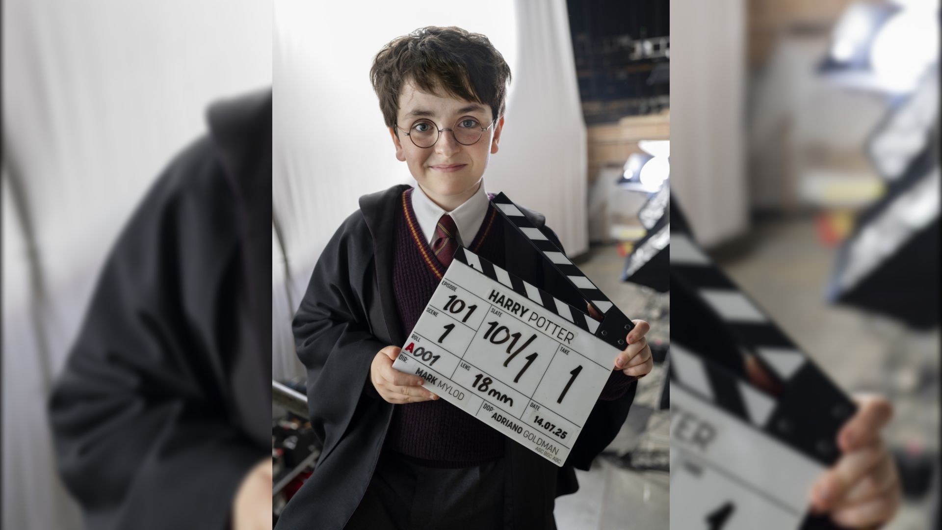 Actorul Dominic McLaughlin în mantie neagră și ochelari ține o clapetă de film