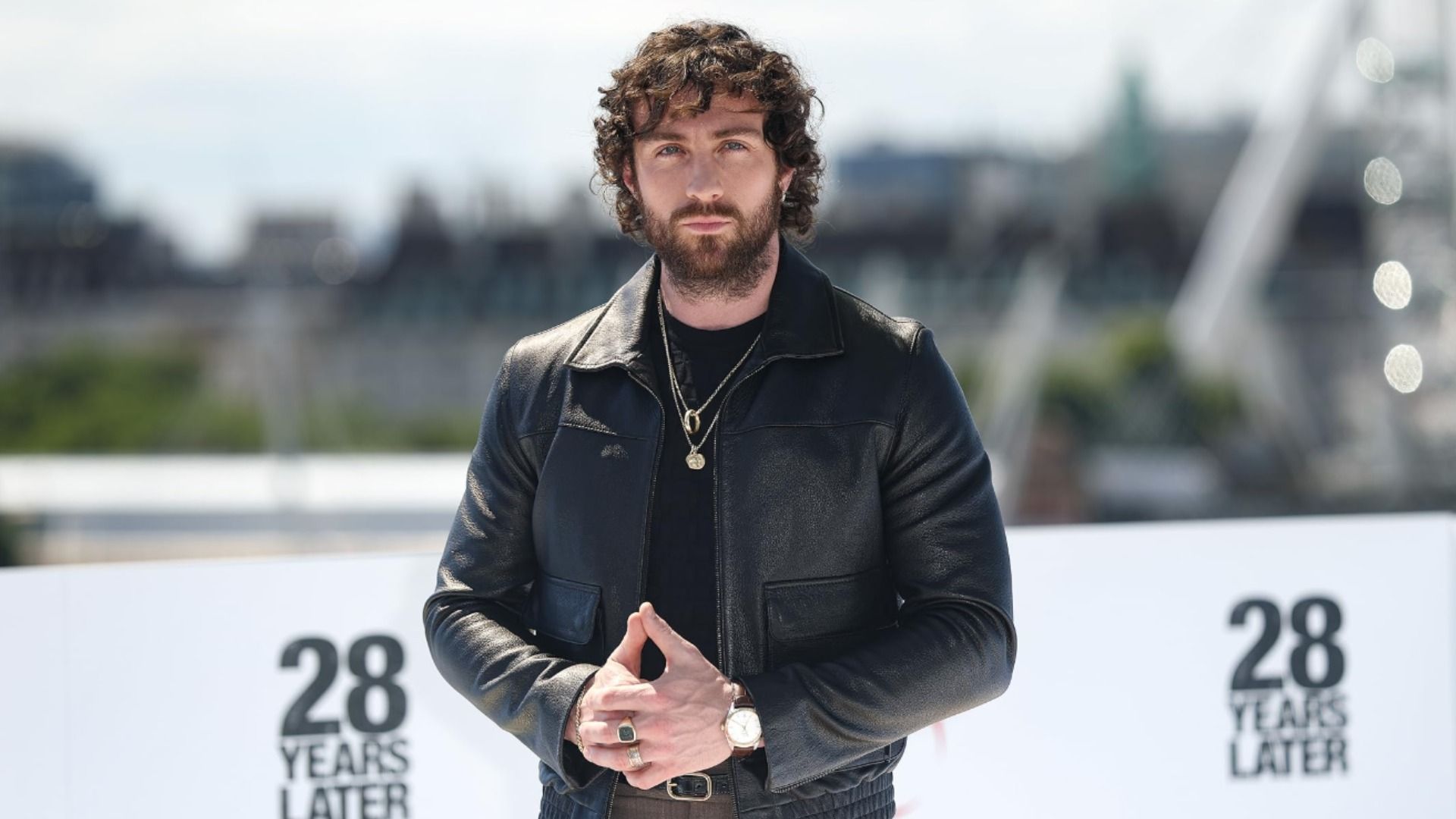 Actorul Aaron Taylor-Johnson într-o jachetă de piele neagră stă pe un fundal urban estompat