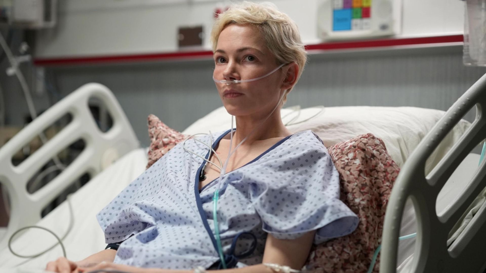 Actrița Michelle Williams în haine de pacient de spital zace pe un pat cu un tub în nas