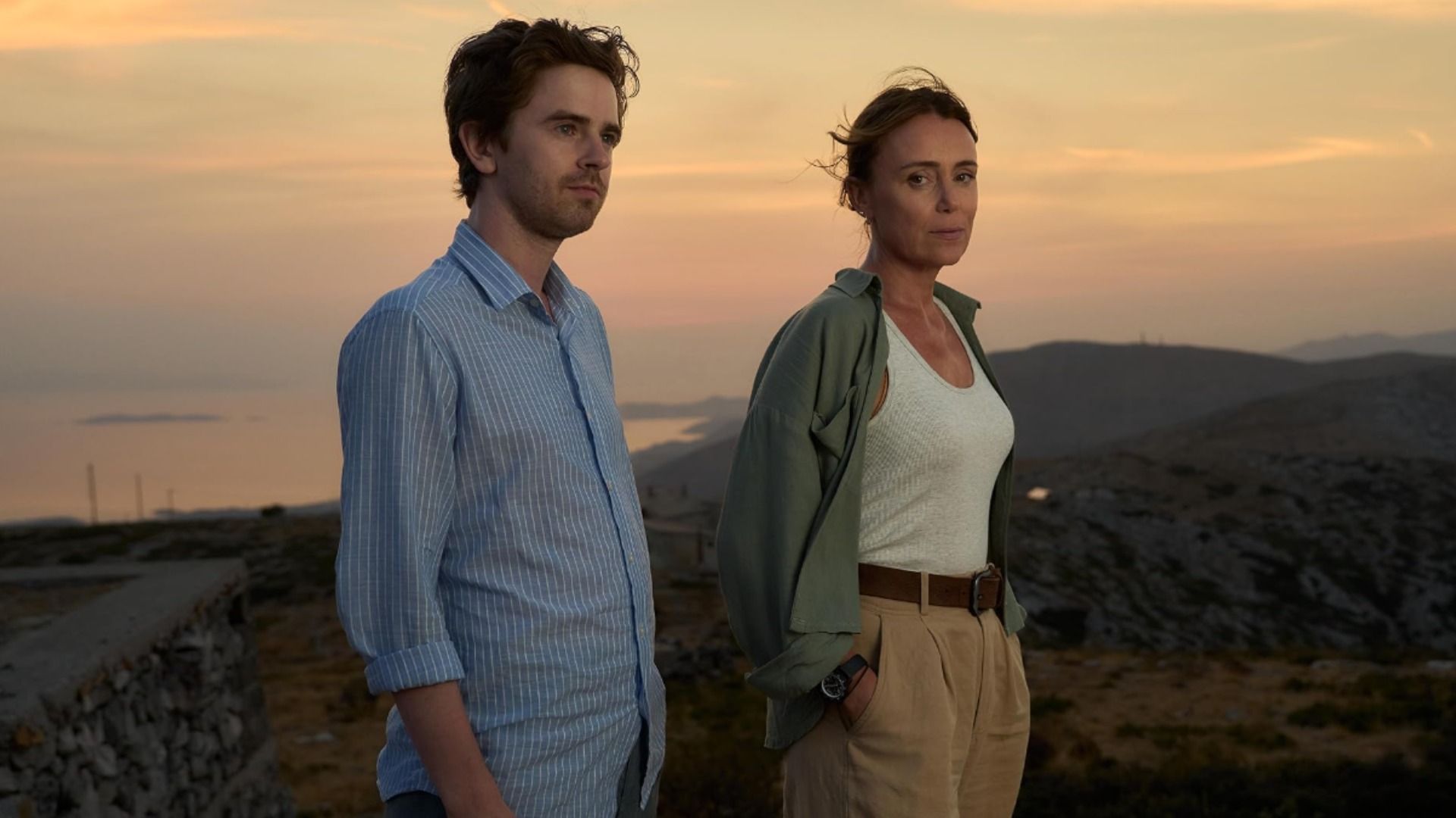 Actorul Freddie Highmore într-o cămașă albastră și actrița Keeley Hawes într-un tricou alb stând pe fundalul unui munte